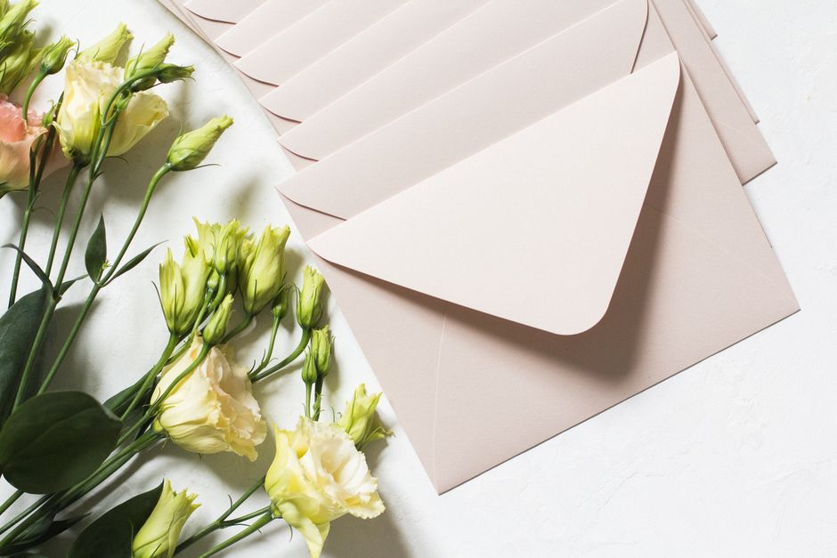 A collection of fresh flowers including pale yellow and cream carnations with ruffled petals and pale green buds, arranged alongside slender green stems and leaves. The flowers are placed on a white s