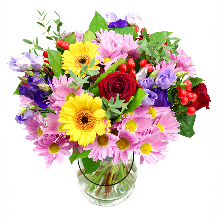 A tall glass vase brims with a mixed bouquet bursting with colour, poised before a smooth white background so that every detail of the flowers is clearly defined, much like a showcase piece in an Eastcote shop window. In the centre sit sumptuous deep red roses, their velvety petals spiralling inwards, adding depth and a timeless, romantic note. Beside them, two bold yellow gerbera daisies with warm brown-orange centres reach outwards, their layered petals forming perfect circles that radiate cheerful energy. Surrounding this focal cluster is a generous ring of soft pink and pale lavender chrysanthemums or daisies; each head is made up of many fine petals and a tiny yellow centre, lending the arrangement a softly textured, cloud-like quality. Threading through these blooms are stems of purple and lilac lisianthus, some flowers open and bell-like, others still in elegant buds, which introduce a cool, sophisticated contrast and gentle vertical movement. Bright red hypericum berries punctuate the design in small, rounded clusters, adding depth, playful accents, and a slightly woodland feel. A variety of greens frame and support the flowers - broad, deep-green leaves provide structure, while lighter, airy foliage creates a natural, just-picked freshness, as if the bouquet were gathered from a secluded Eastcote garden near the Yeading Brook. The clear vase reveals a neat fan of stems submerged in sparkling water, showcasing the careful hand of an experienced florist. Overall, the arrangement feels joyful, generous, and uplifting, perfectly suited for marking milestones, saying thank you, or simply brightening a kitchen table in an Eastcote home with warmth and colour.